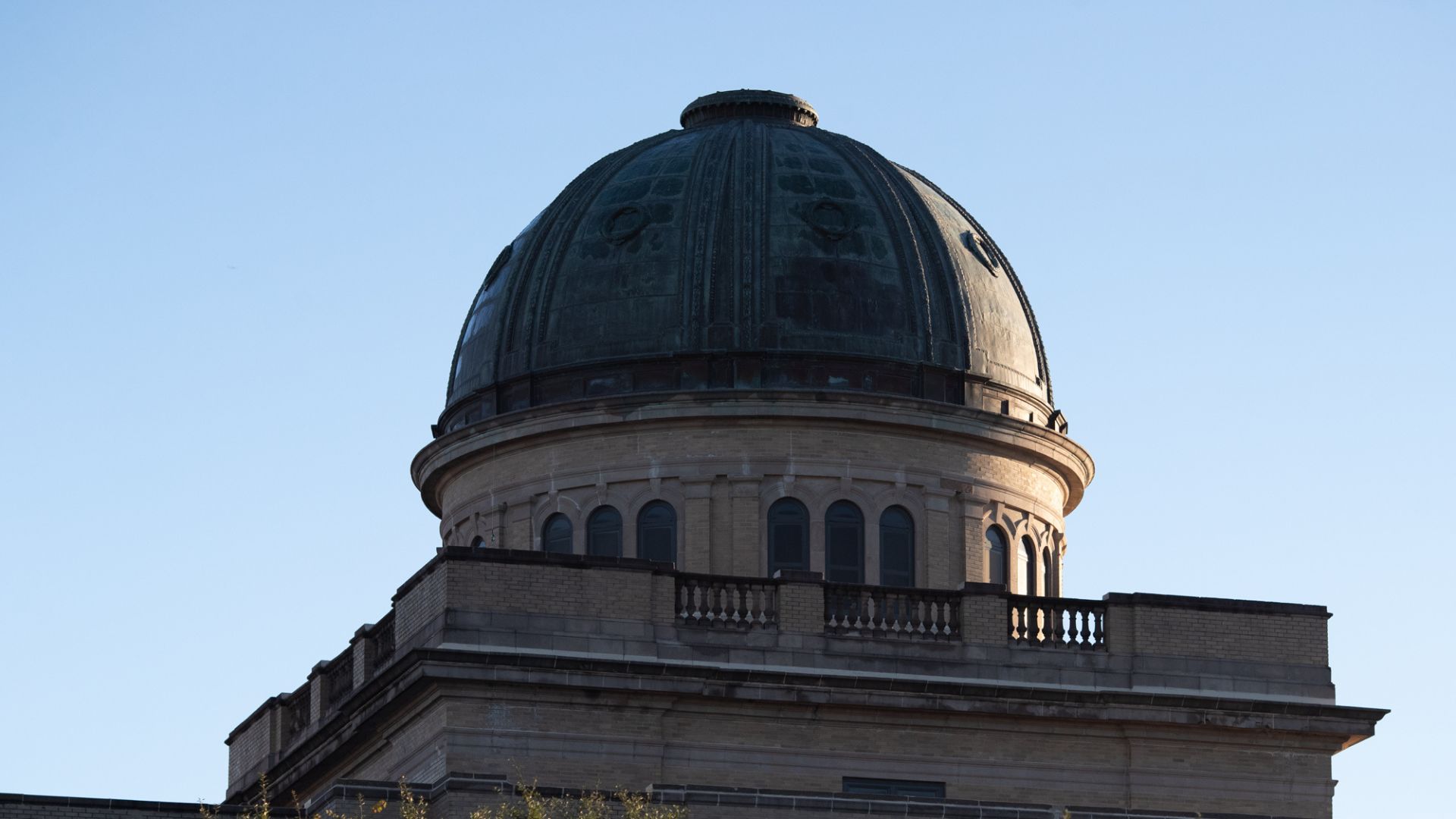 The dome of a Academic Building is photographed against a clear blue sky, highlighting its architectural details.